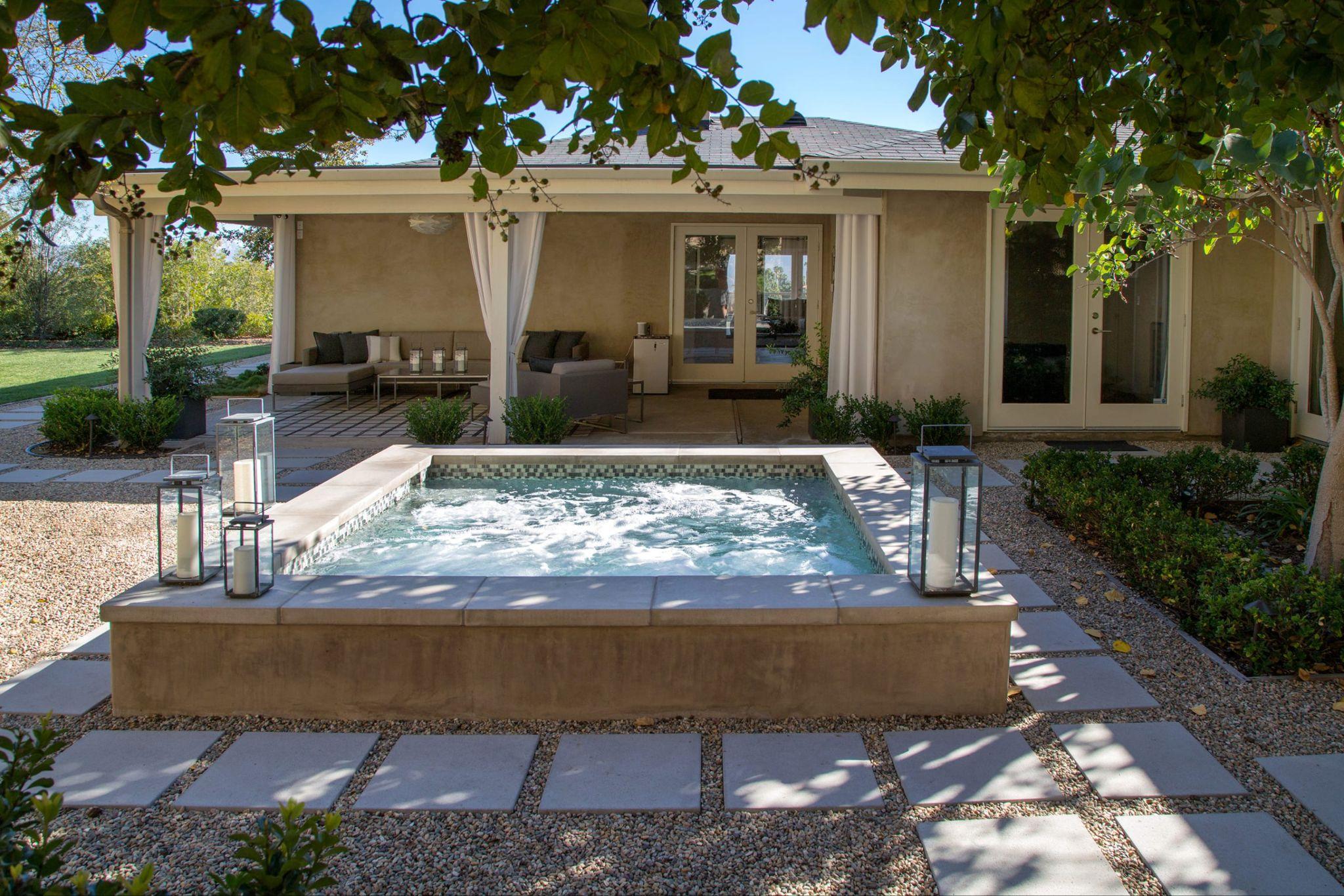 Contemporary outdoor spa with bubbling water, minimalist stone coping, and a shaded lounge seating area surrounded by greenery.