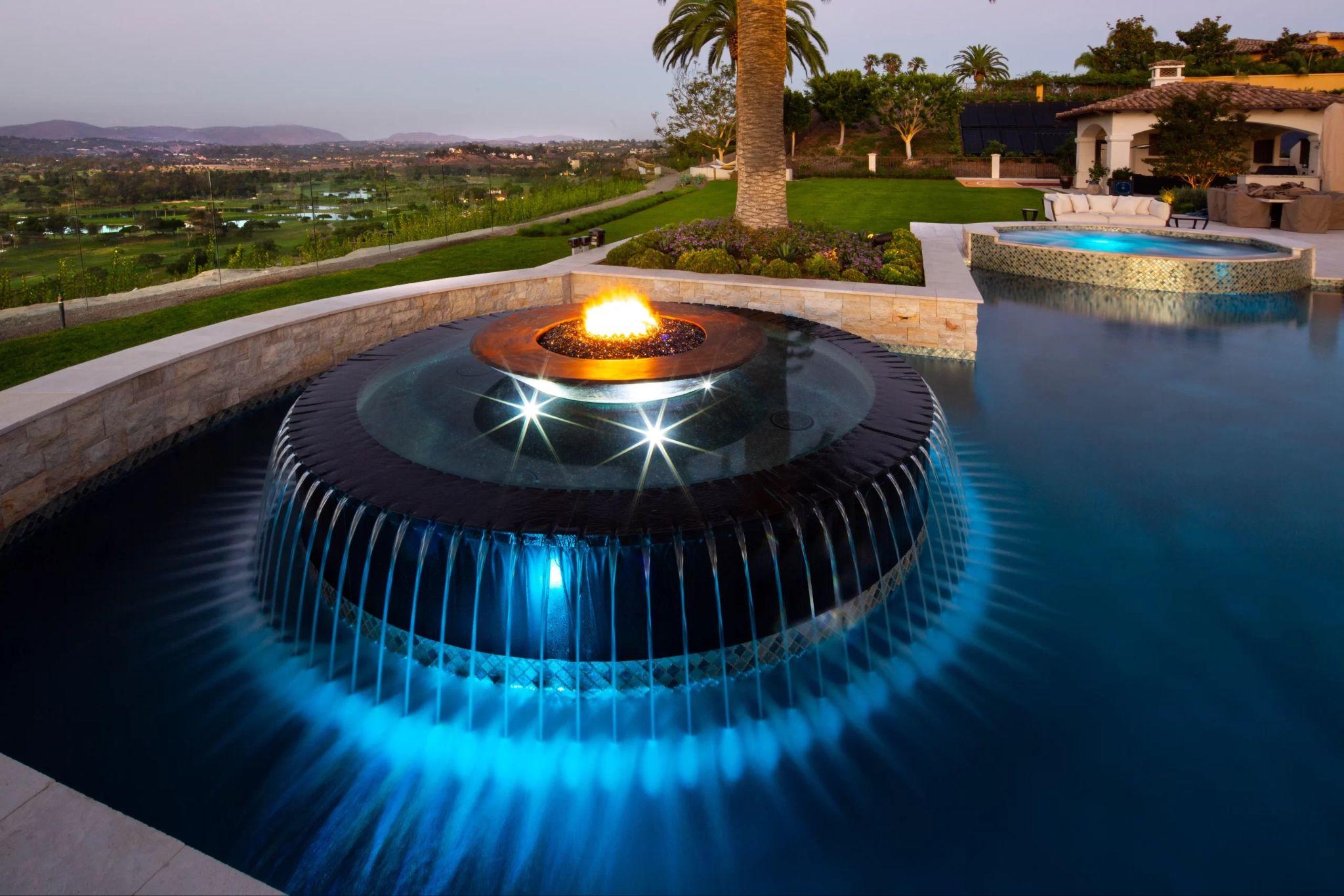 Dramatic circular waterfall with a central fire feature glowing at dusk