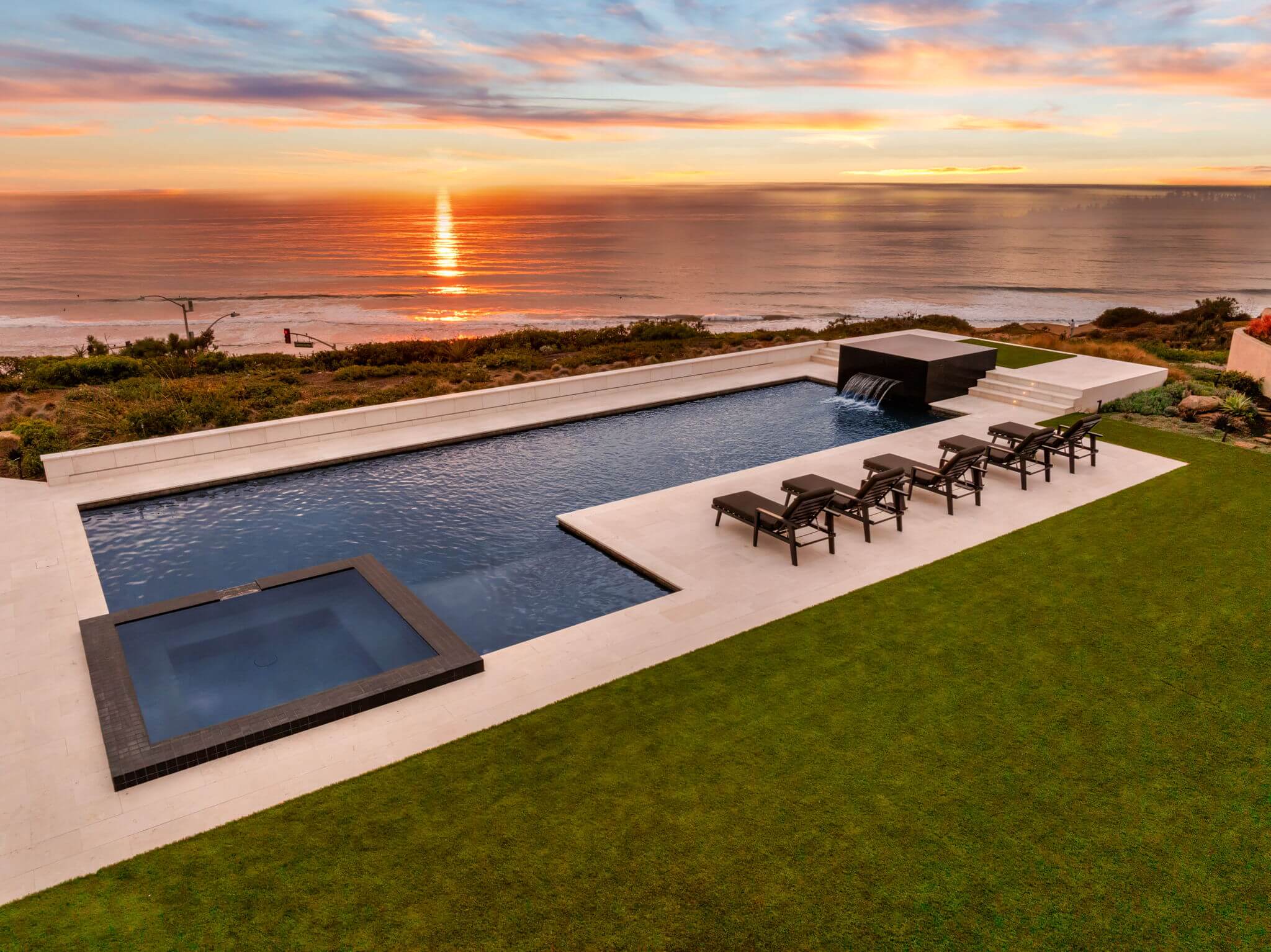 Sleek oceanfront pool with raised spillover spa and loungers at sunset.
