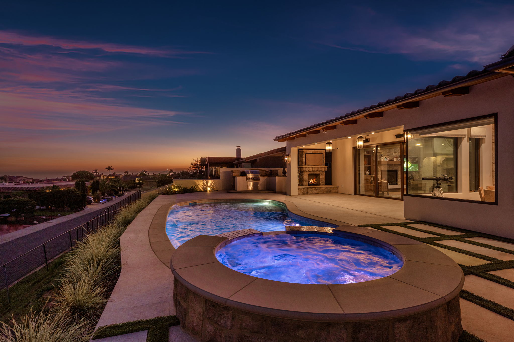 Luxury pool with raised spa and outdoor fireplace at twilight