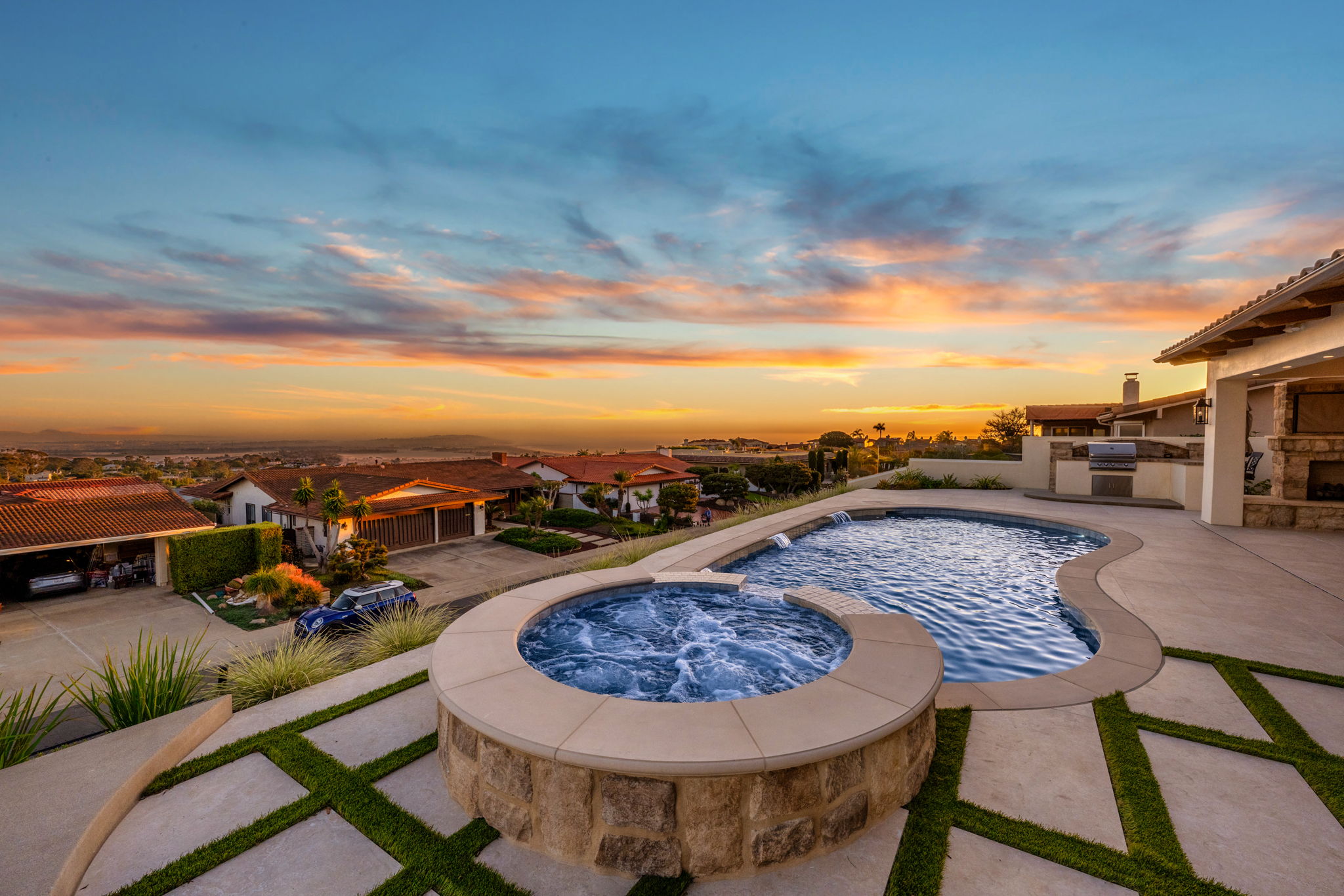 Freeform concrete pool with raised spa and hillside sunset view.