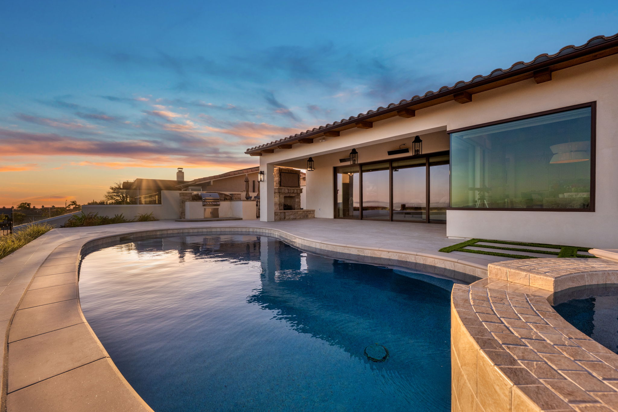 Custom curved pool and spa with outdoor kitchen at sunset