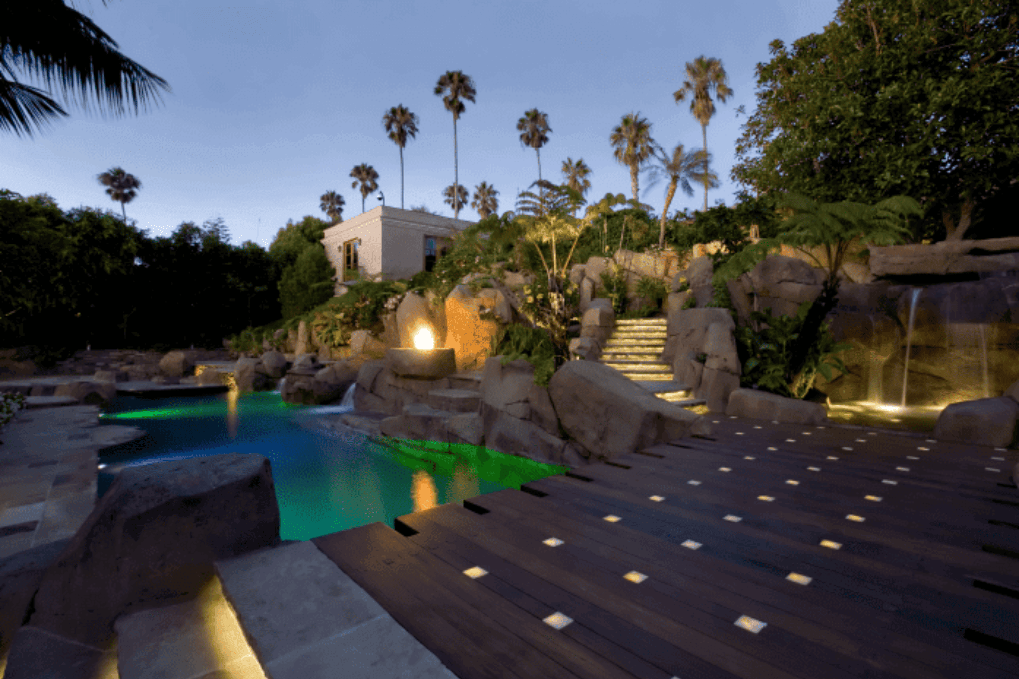 A wooden deck overlooking a luxury pool lit with ambient lighting