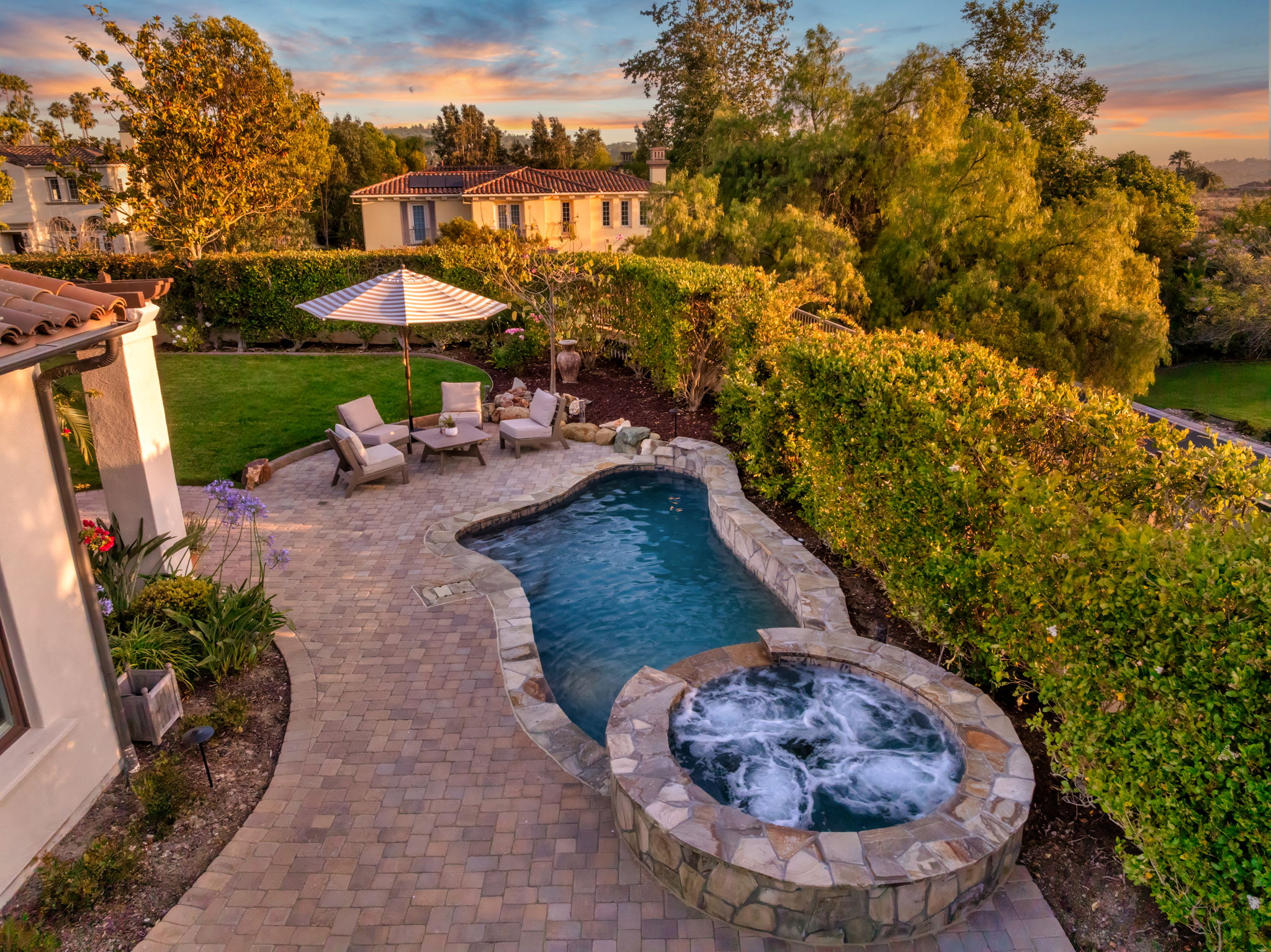 Freeform pool with stone spa and paver deck at sunset