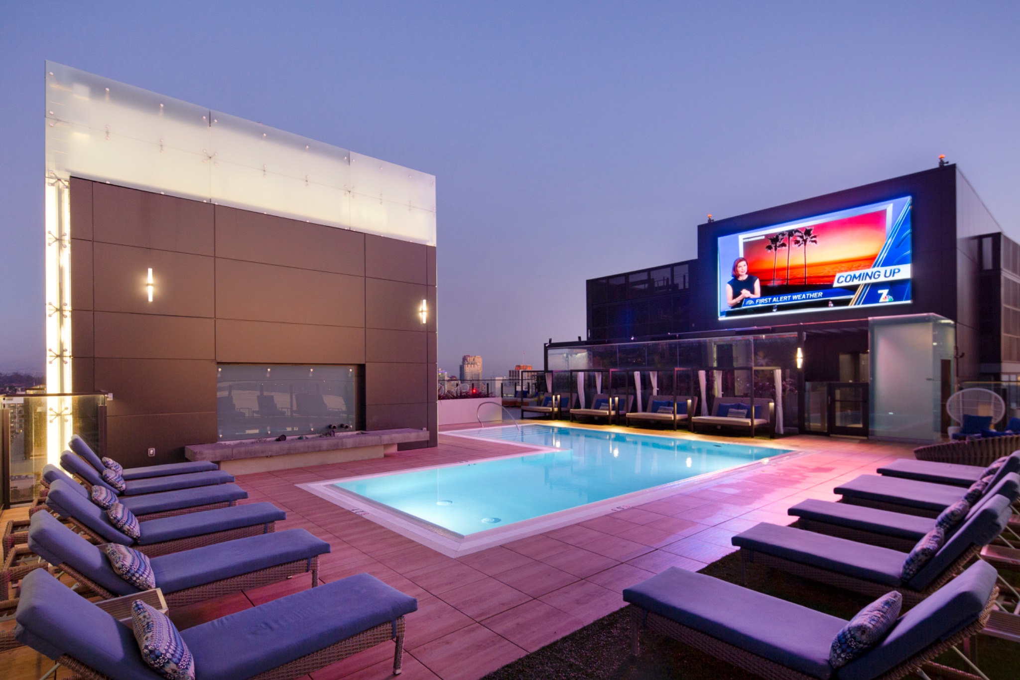 Rooftop pool with lounge seating and screen at dusk