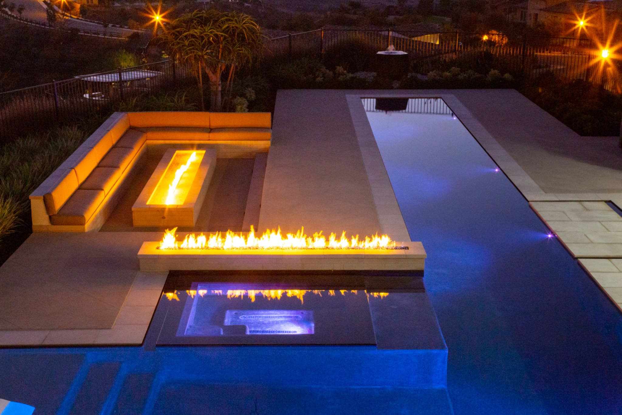 Linear fire features paired with sunken seating beside an LED-lit pool, a resort-style pool upgrade idea for evening entertaining