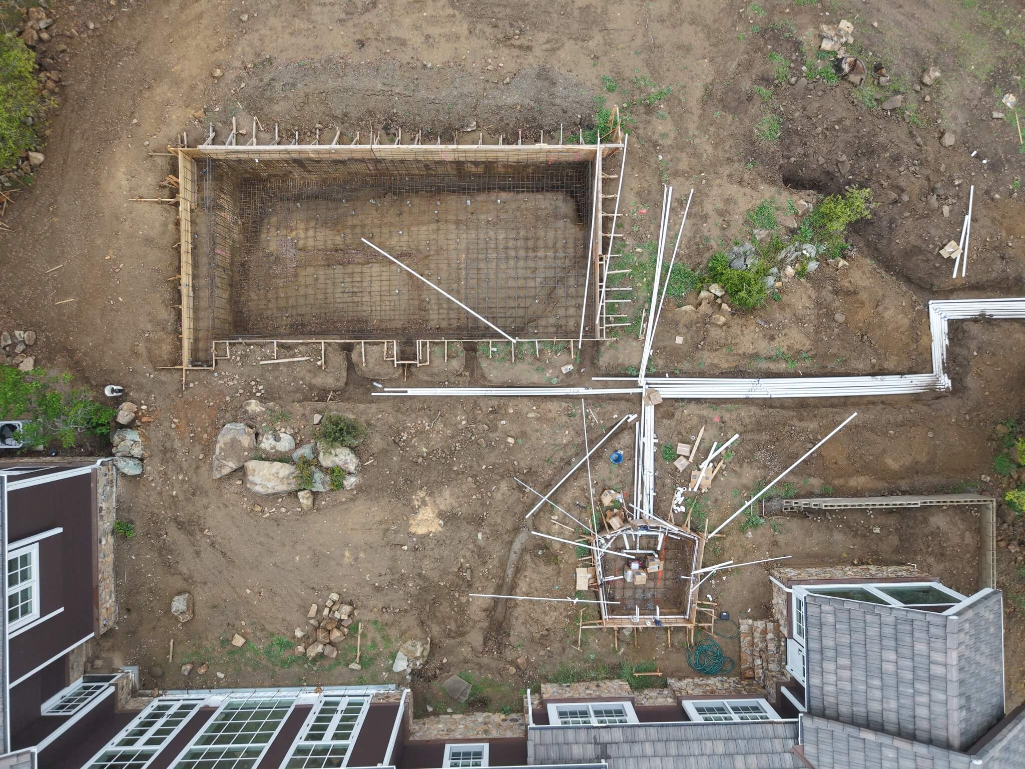 Overhead view of swimming pool renovation showing rebar cage, plumbing lines, and spa structural framework before shotcrete