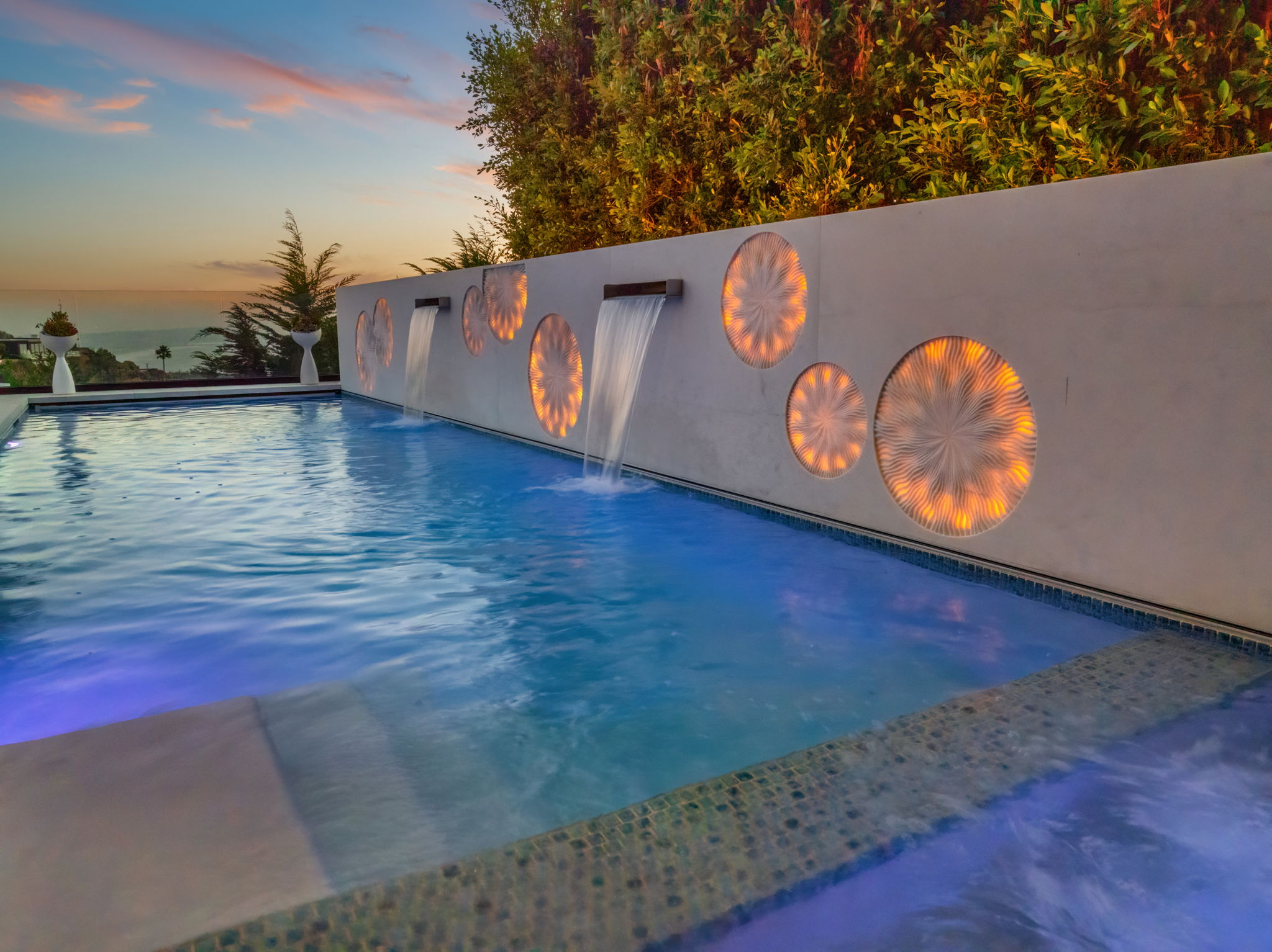 Pool water feature wall with sheer-descent waterfalls and illuminated medallions, two high-impact pool renovation ideas