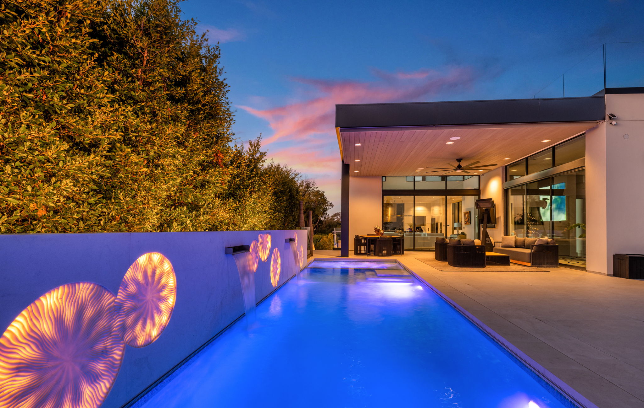 Color-changing LED pool lighting and illuminated wall features at twilight, a popular backyard pool renovation upgrade